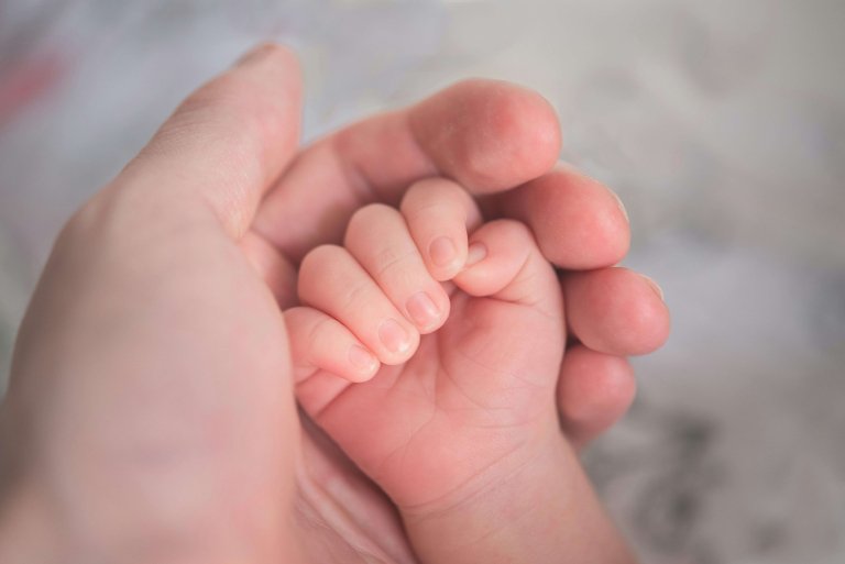 an intended parent holding their surrogate baby's hand after a successful surrogate journey