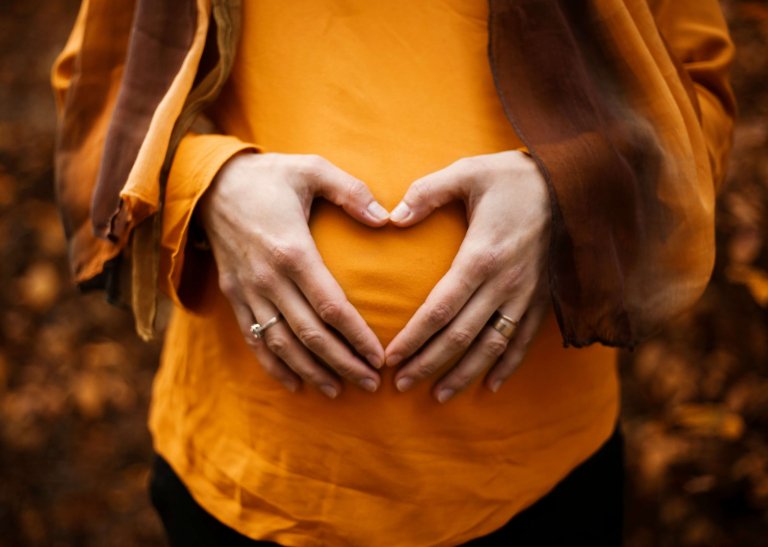 a surrogate making a hear with her hands over her womb